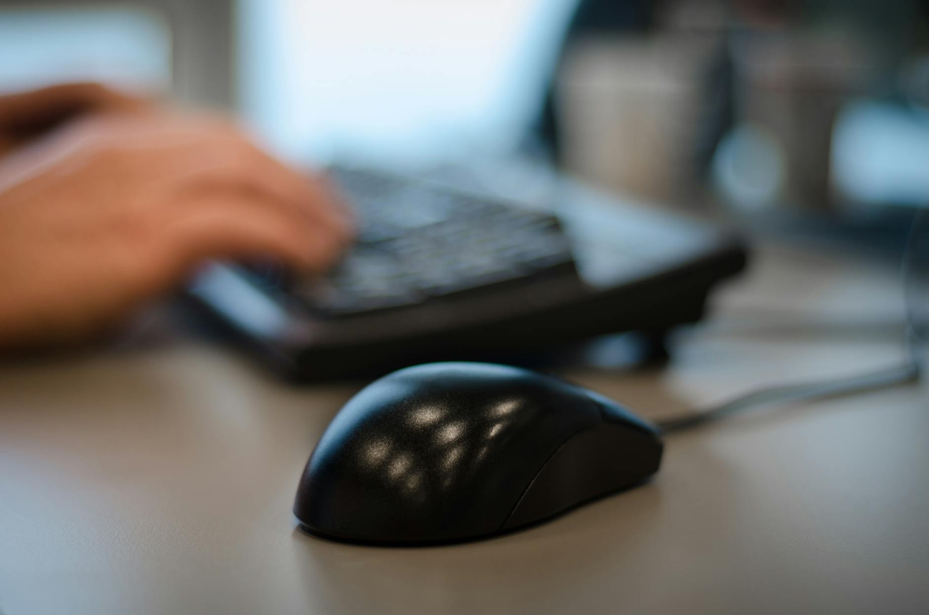 Mouse e tastiera in primo piano su scrivania moderna con dita che digitano